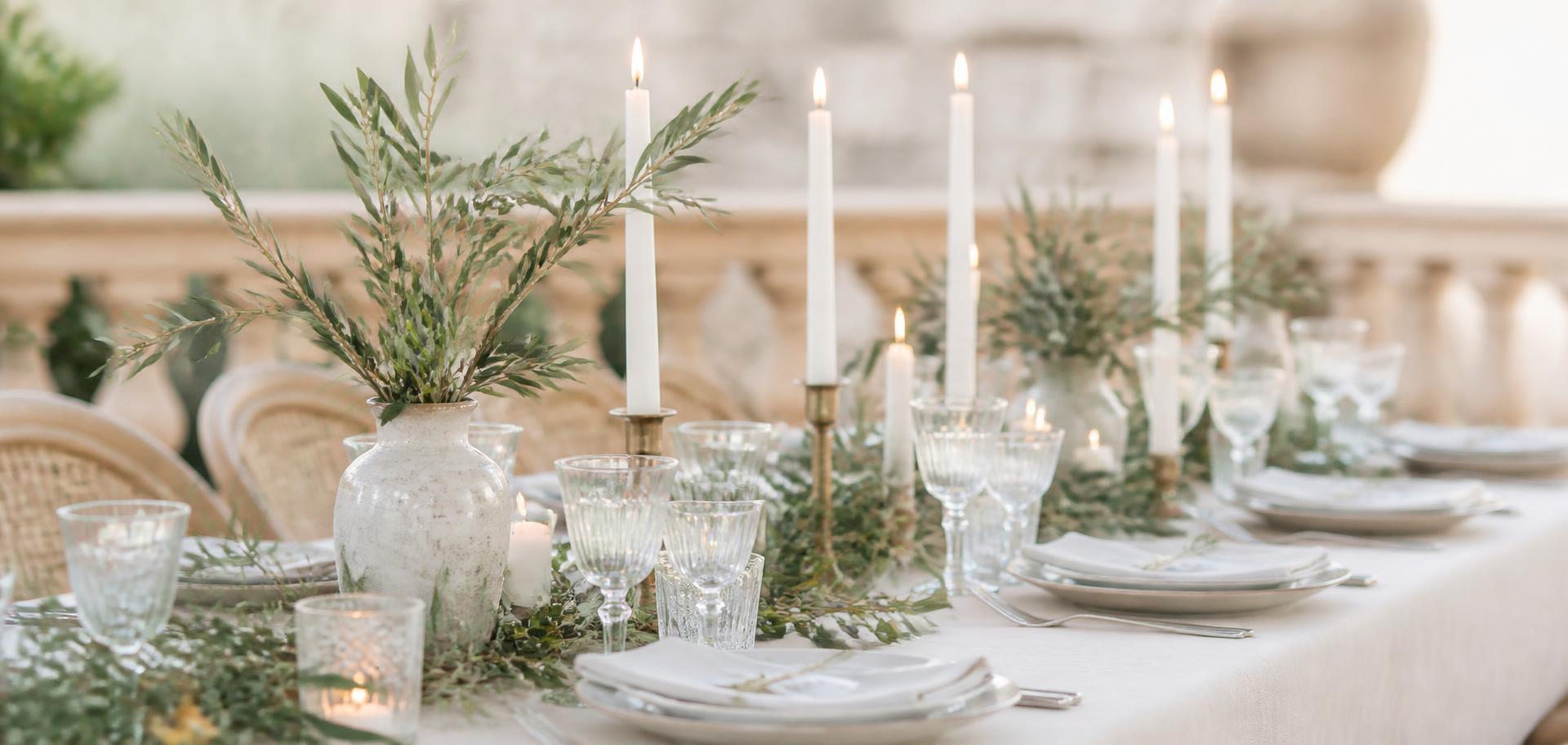 A calm Mediterranean desk with wedding papers, an olive sprig and a linen notebook